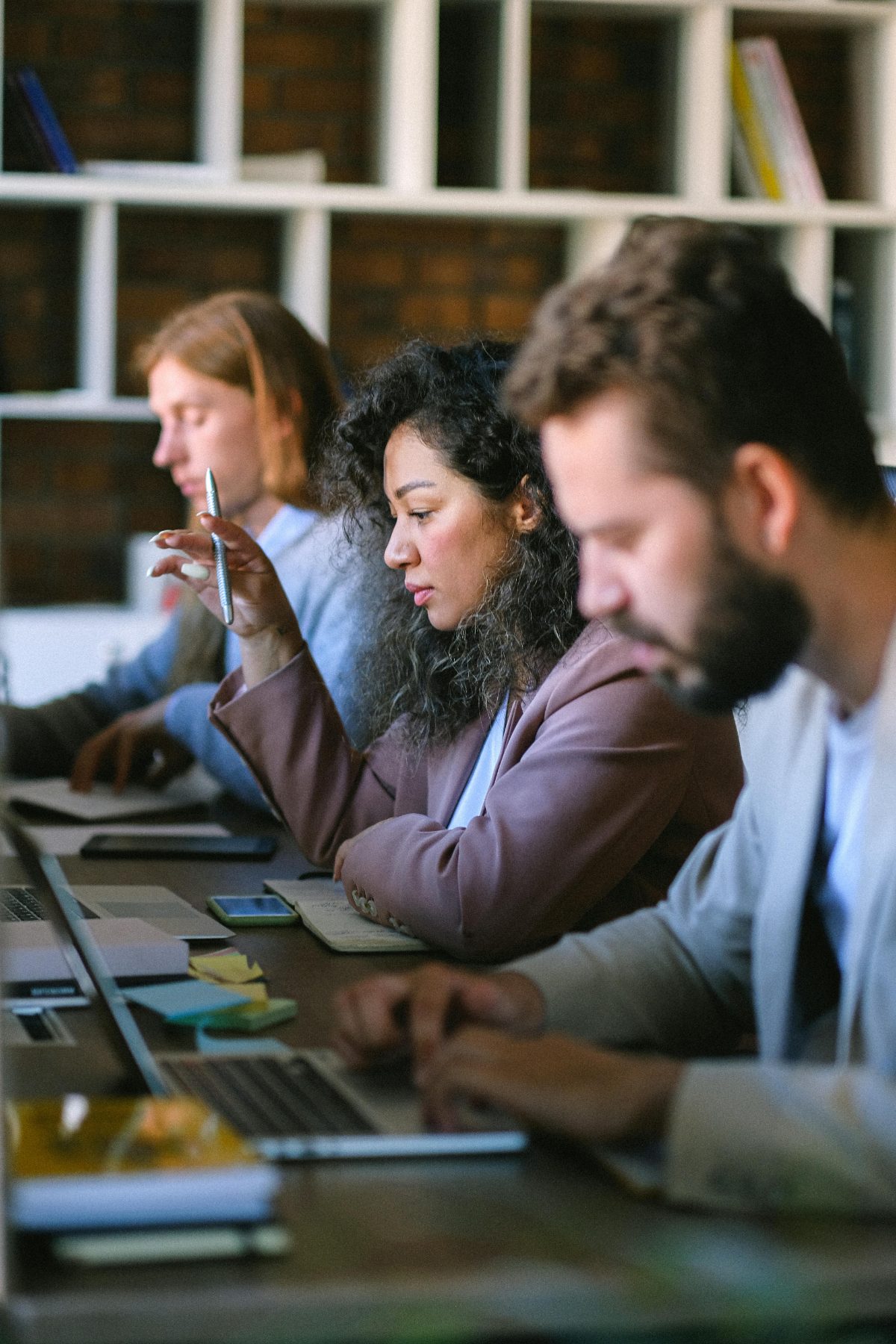Three colleagues are working intently at a table behind their laptops.