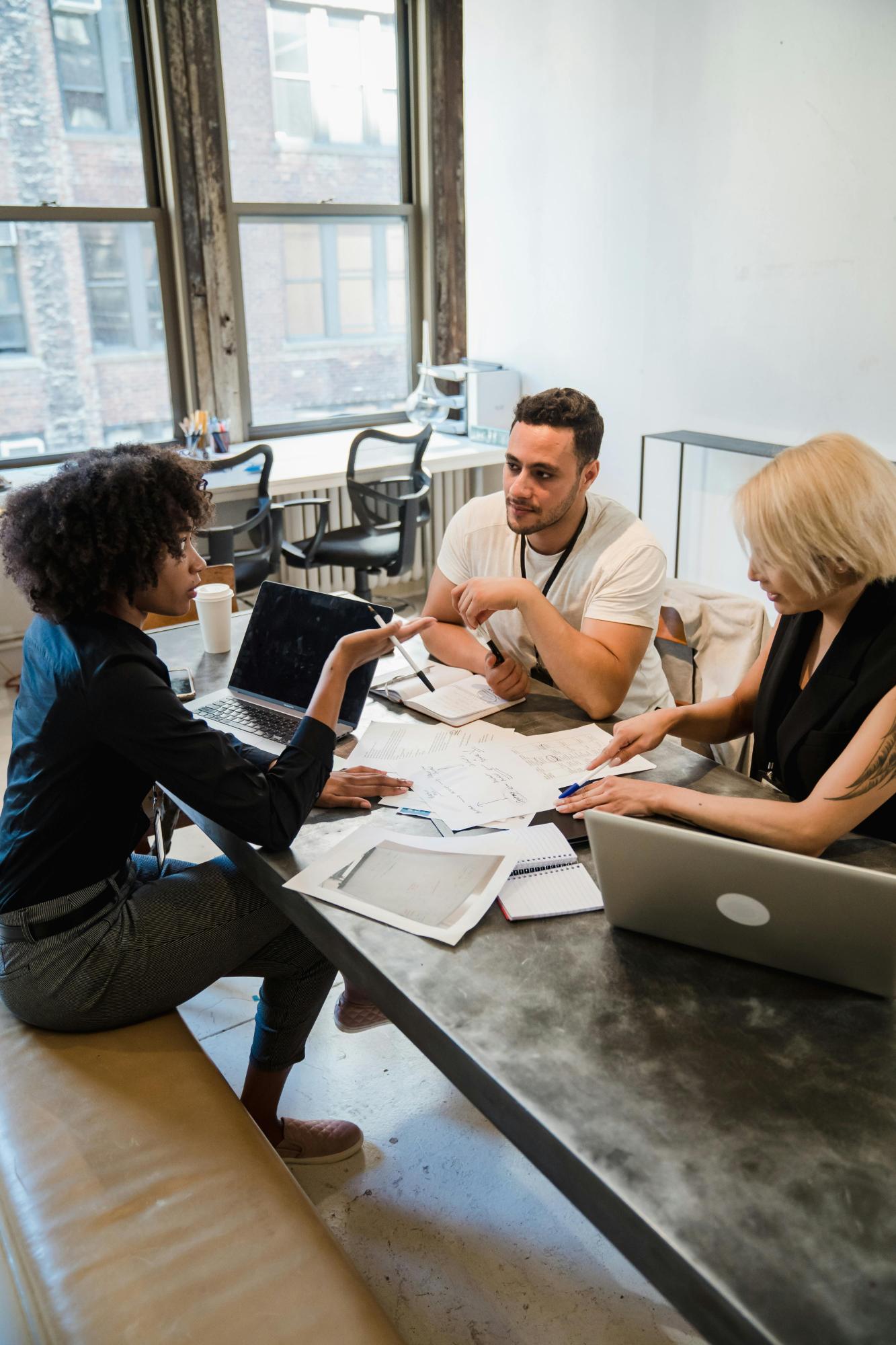 Three colleagues conferring at a table with laptops and documents.