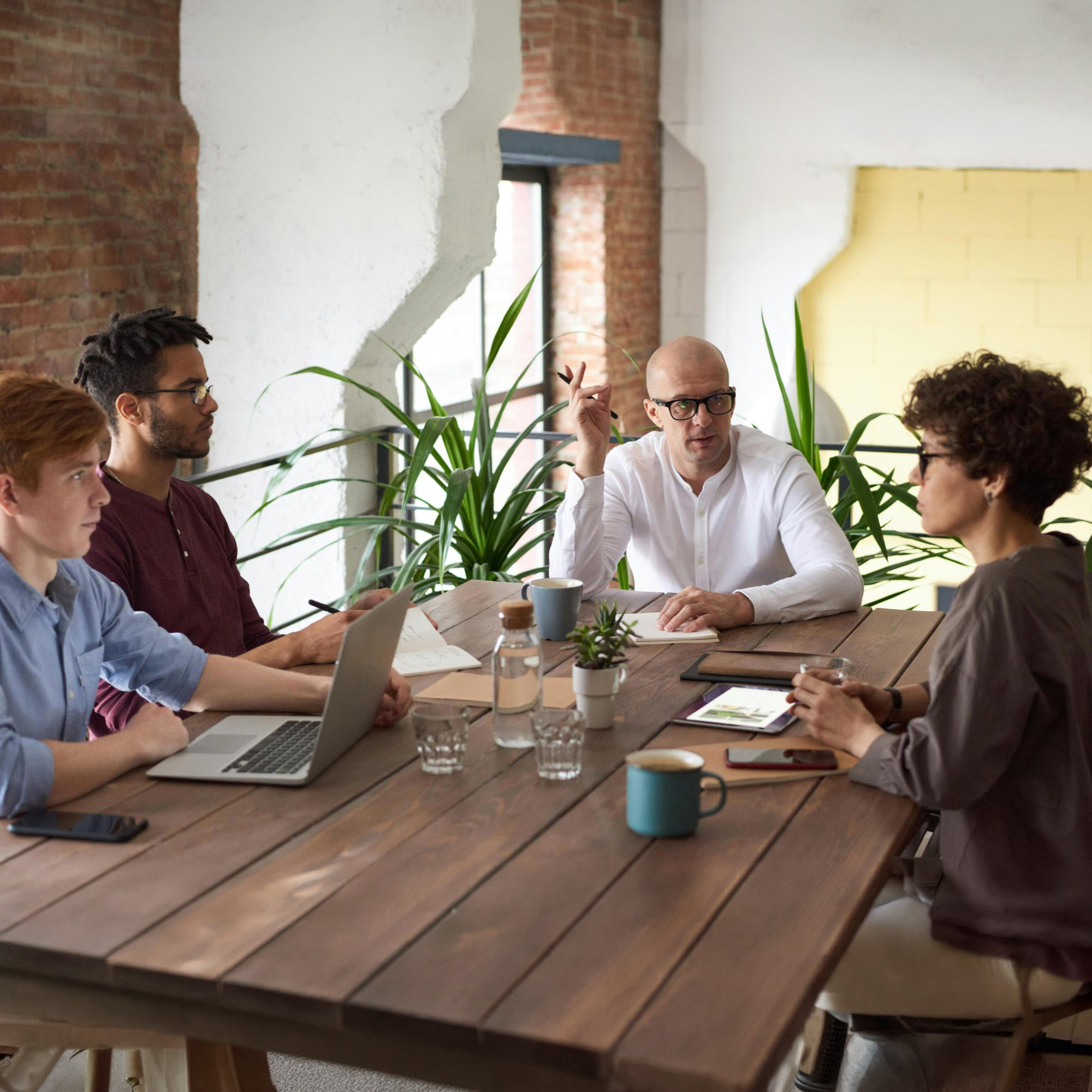 Team meeting at a table in an office with a brick wall and plants.
